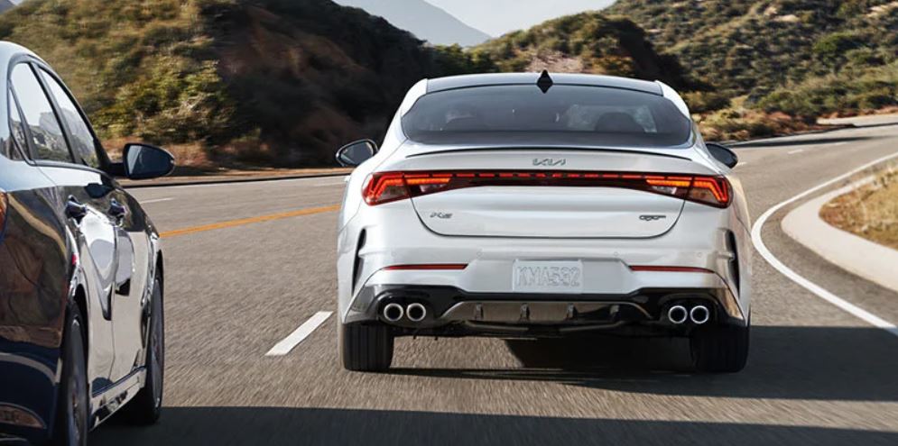Rear view of a white 2022 Kia K5 being driven on the highway with mountains up ahead. | Kia dealer in Conway, AR.