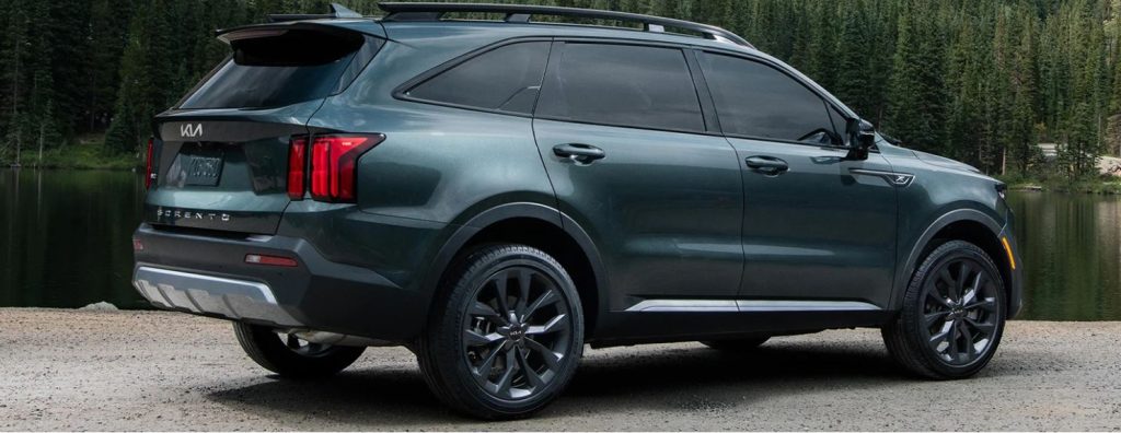 Profile view of a dark bluish-green 2022 Kia Sorento parked in front of a body of water with trees in the background. | Kia dealer in Conway, AR.