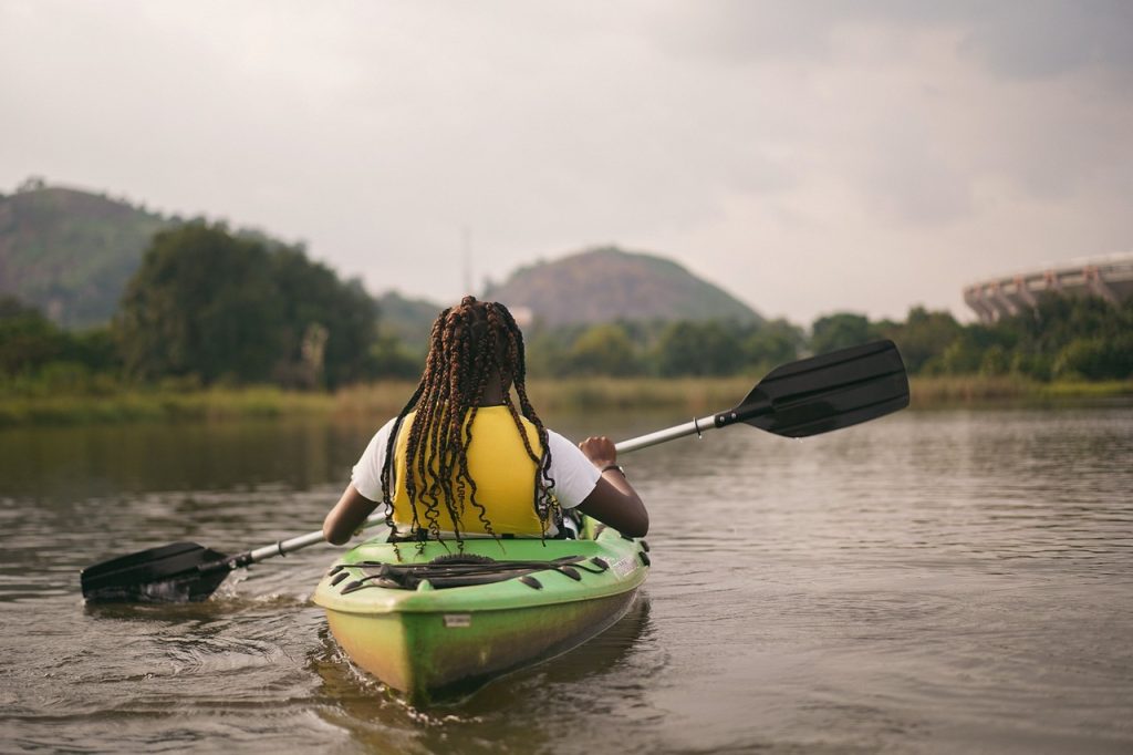 The back of a woman kayaking on a lake with trees and hills up ahead. | Spring activities near Conway, AR | Crain Kia of Conway